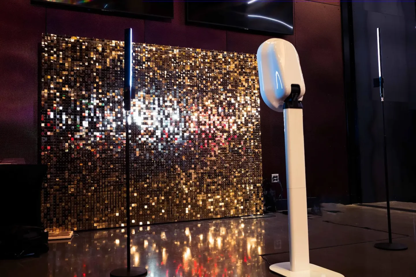 A photo booth setup with a gold sequin backdrop, a camera, and two vertical light stands.