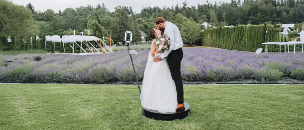 A bride and groom kissing on a small platform in front of the professional photo booth camera