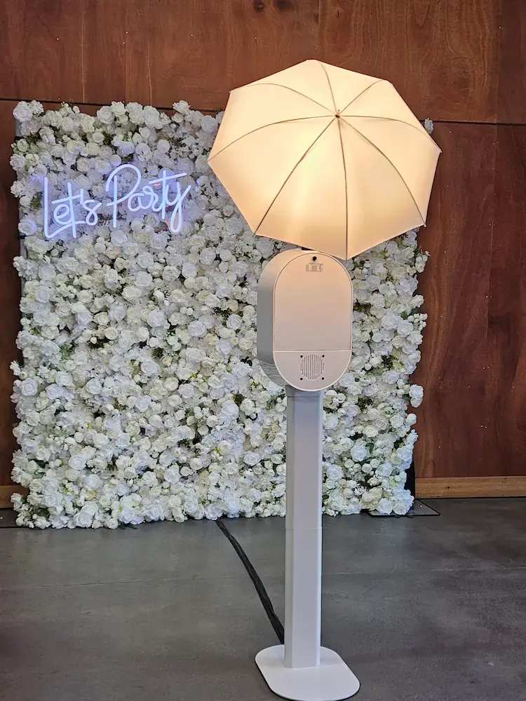 Photo booth with an umbrella light in front of a luxury floral backdrop.