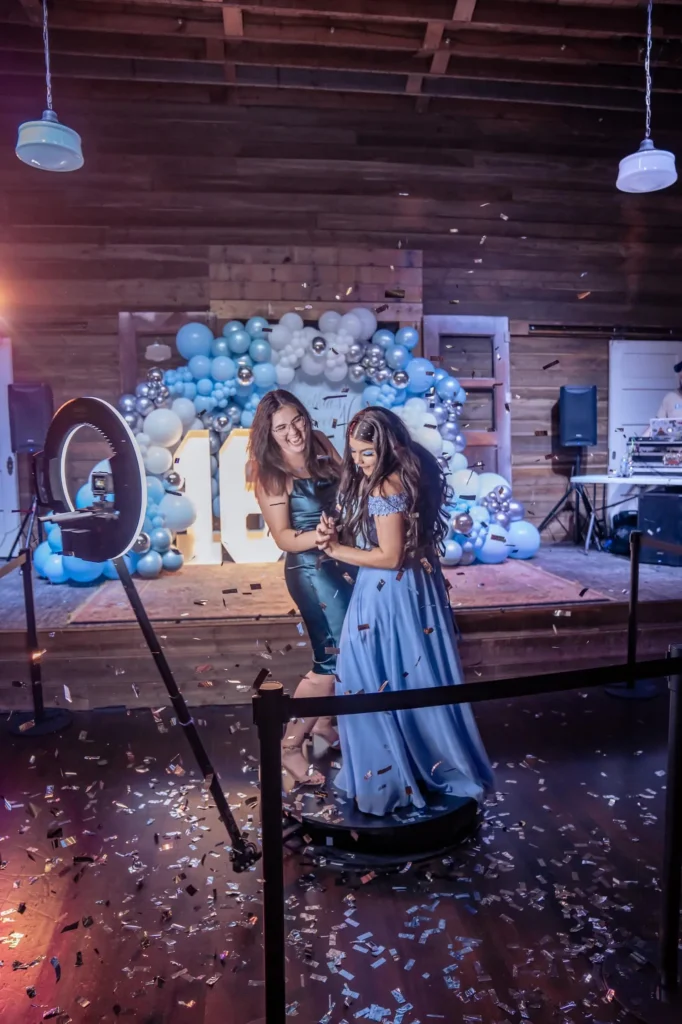 Two women smiling and posing in front of a photobooth stataion camera and lightning.