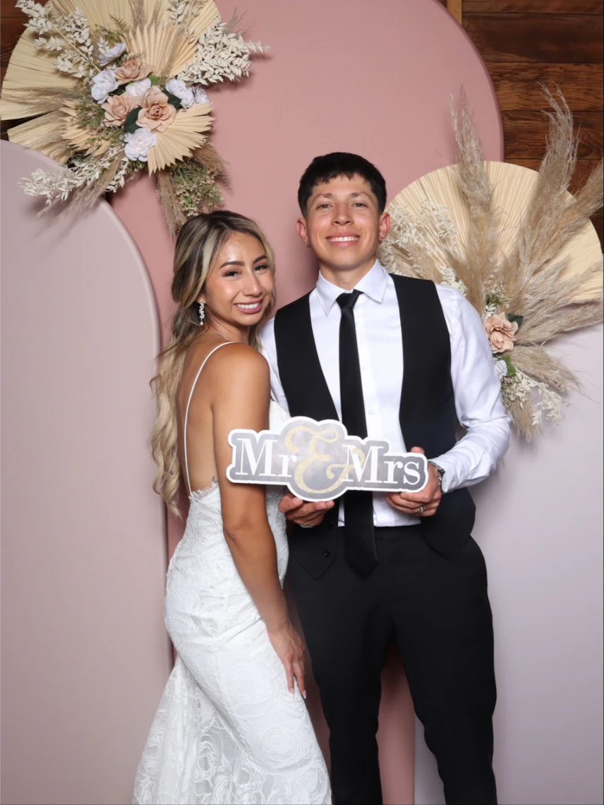 A couple in formal attire poses with a "Mr & Mrs" sign against a decorative backdrop