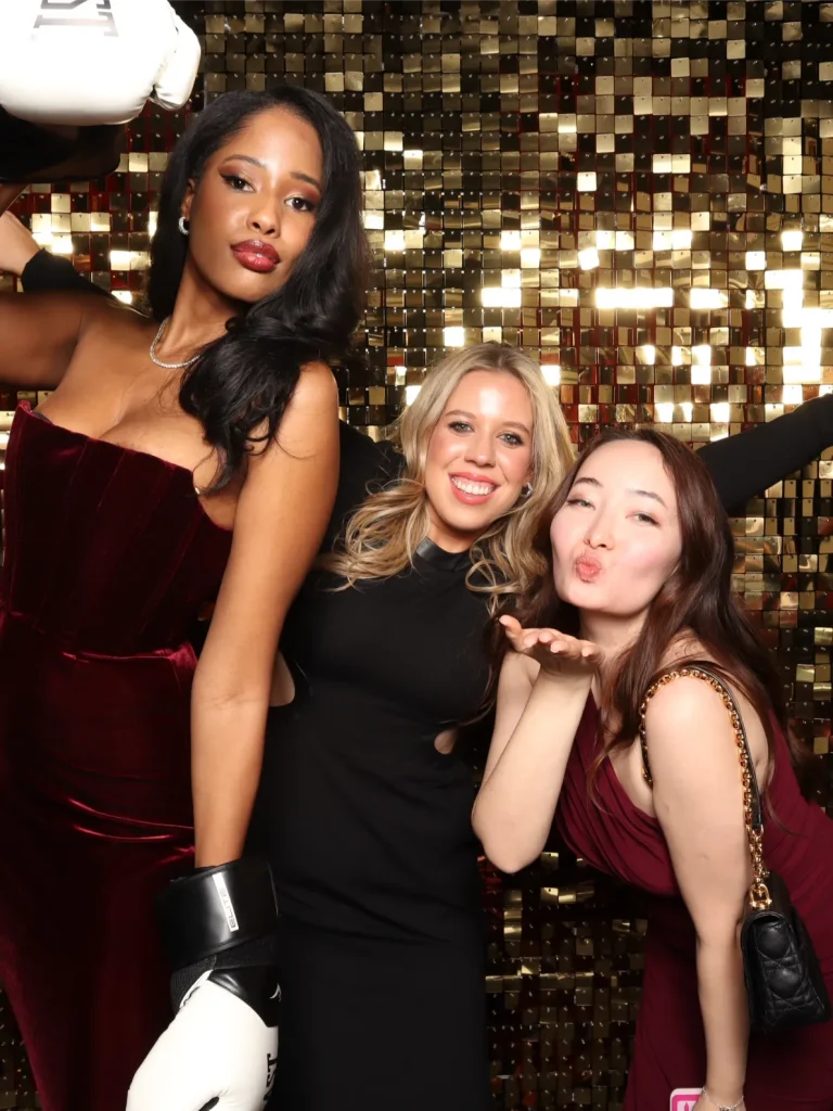 Three women pose in front of a golden sequin backdrop.