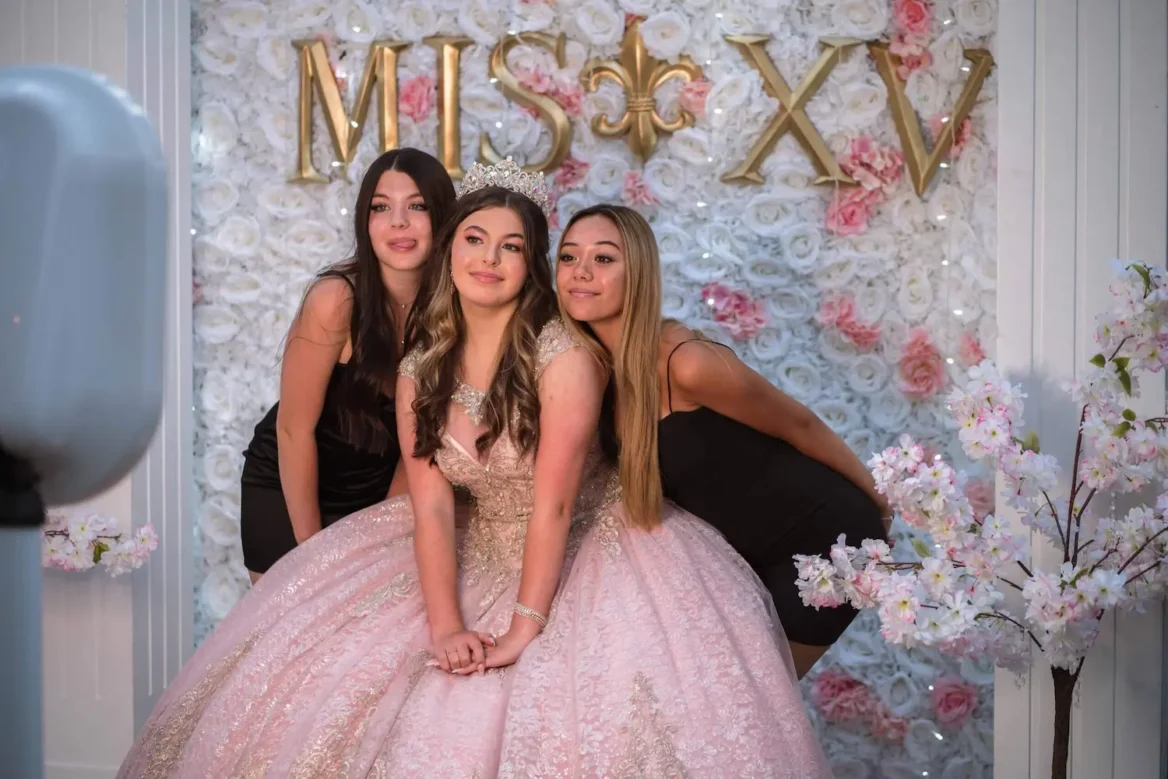 Three young women pose in front of a floral backdrop.