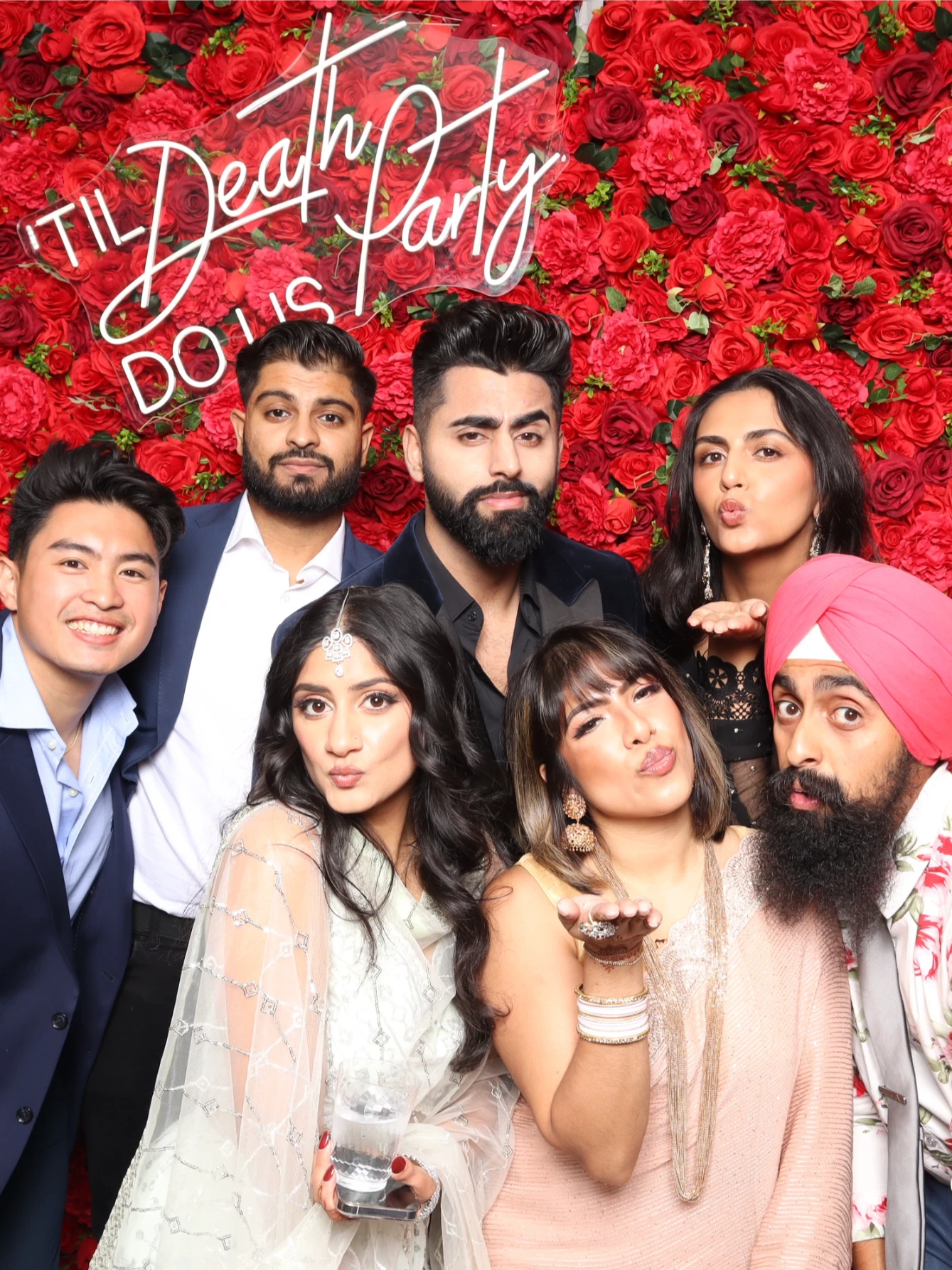 A group of seven people pose in front of a red rose backdrop.