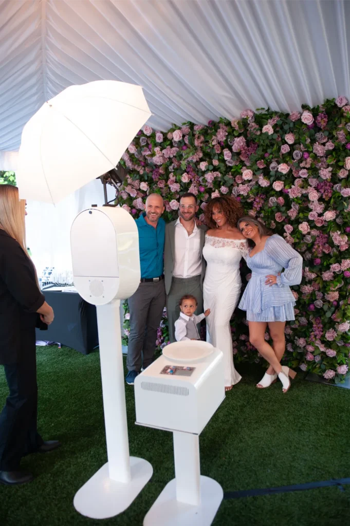 Group of people posing for a photo in front of a floral backdrop under a white tent