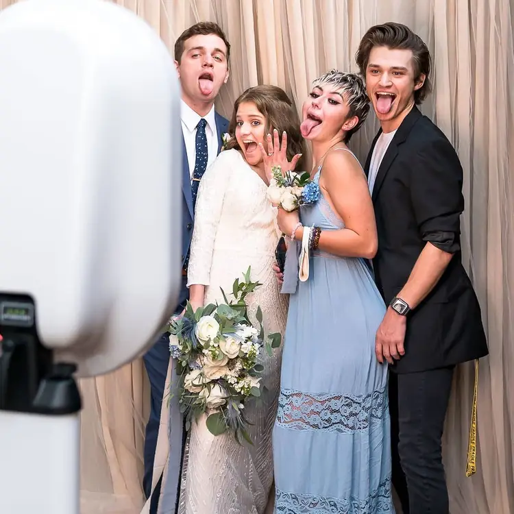 Four people pose in formal attire, smiling in front of a photo booth camera.